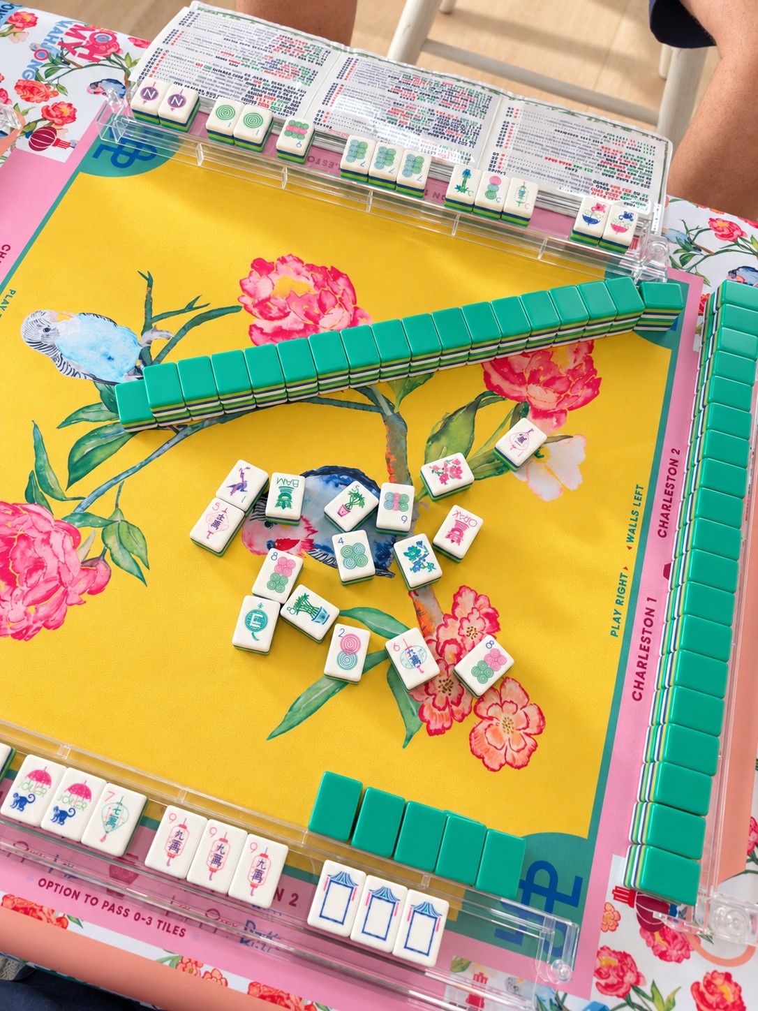 Mahjong tiles and racks on a colorful botanical playing mat